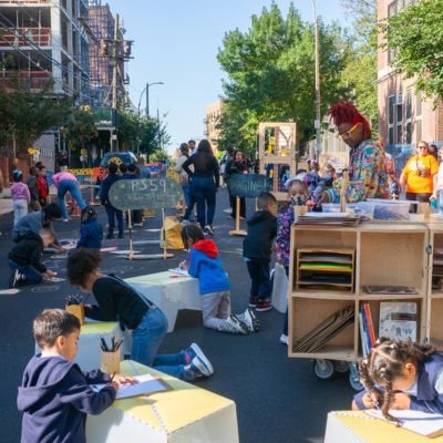 Children draw and color on a street closed to vehicular traffic.