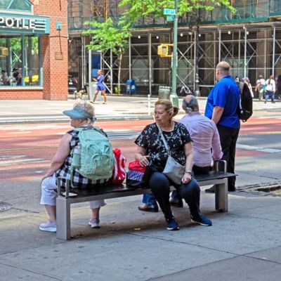 People sit on a public bench near a bus stop.