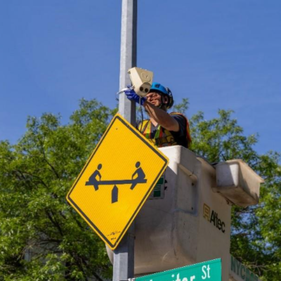 A Department of Transportation worker using a bucket truck installs a sensor above a children at play sign on a streetlight pole in New York City. 
