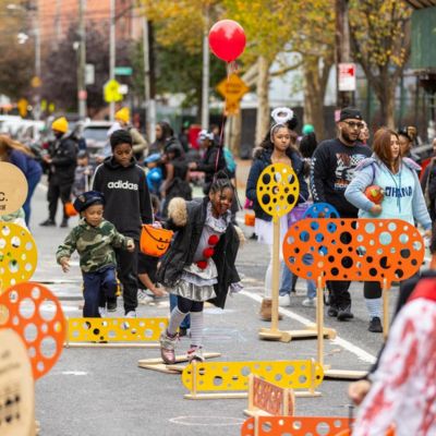 Kids in Halloween costumes enjoy multiple games and activities on a street closed to vehicular traffic.    