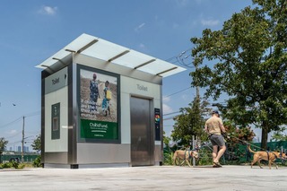 A person with two dogs walk in front of an automatic public toilet in Red Hook, Brooklyn.