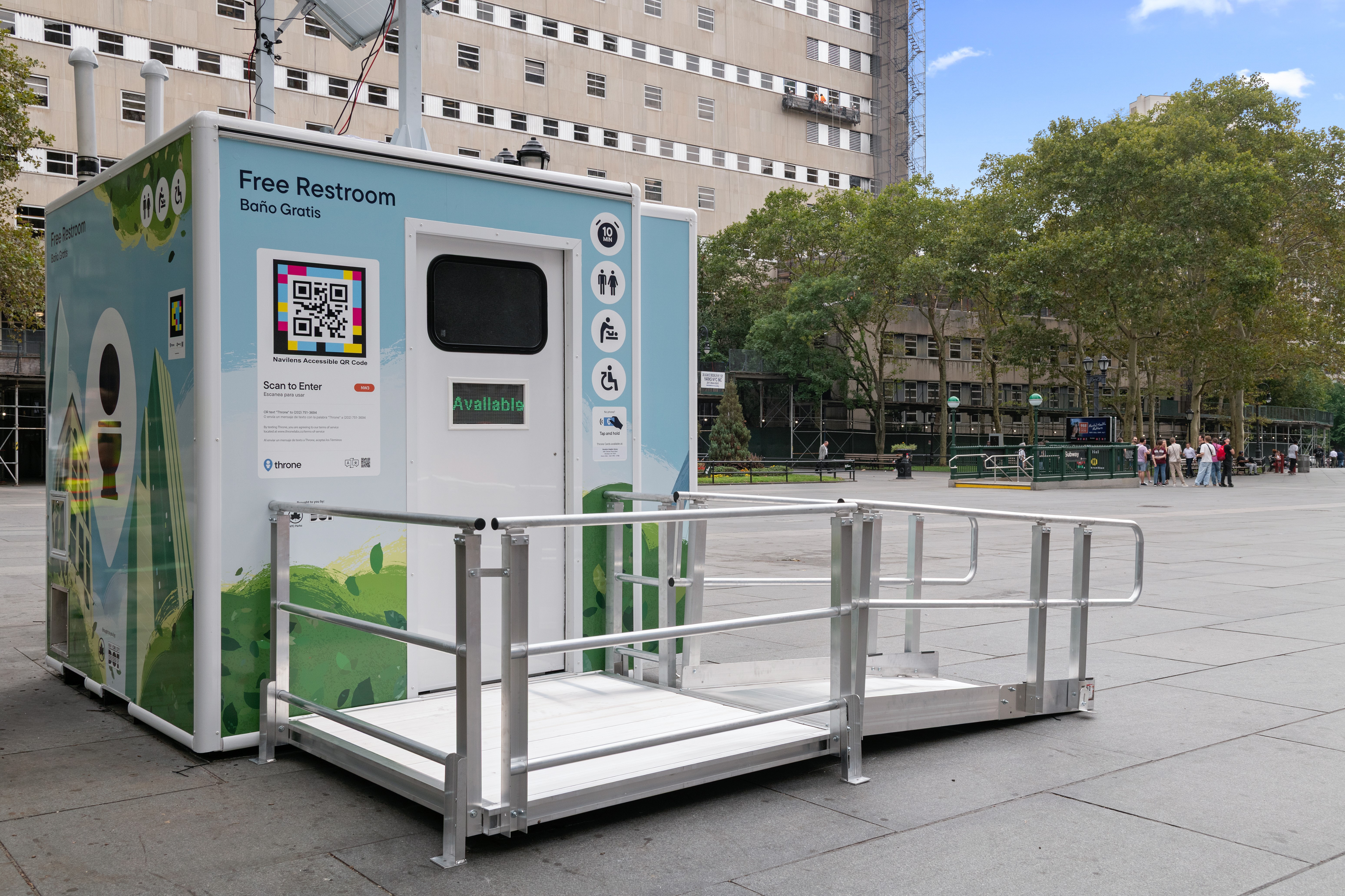 A small building housing a public restroom sits in the middle of a public plaza with a wheelchair accessible ramp leading to the entrance.