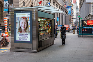 A newsstand on an N Y C sidewalk sells small goods like snacks and magazines.