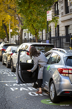 A woman enters a gray car parked on a spot marked as "Carshare Parking Only – Zipcar"