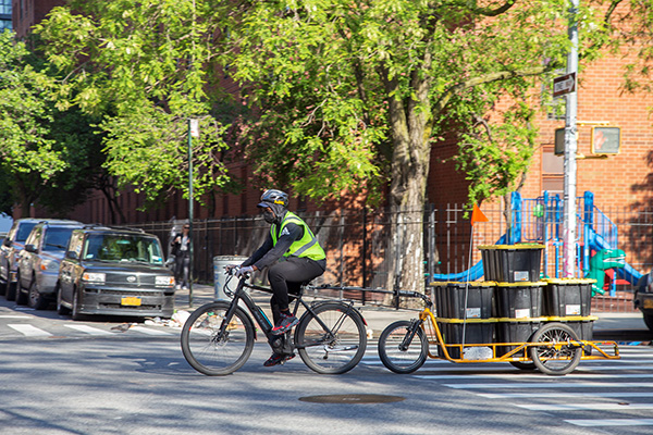 A person rides a bicycle with a cart attached carrying crates.