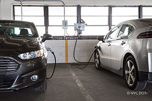 Two electric vehicles are parked inside a municipal lot, plugged into EV chargers.