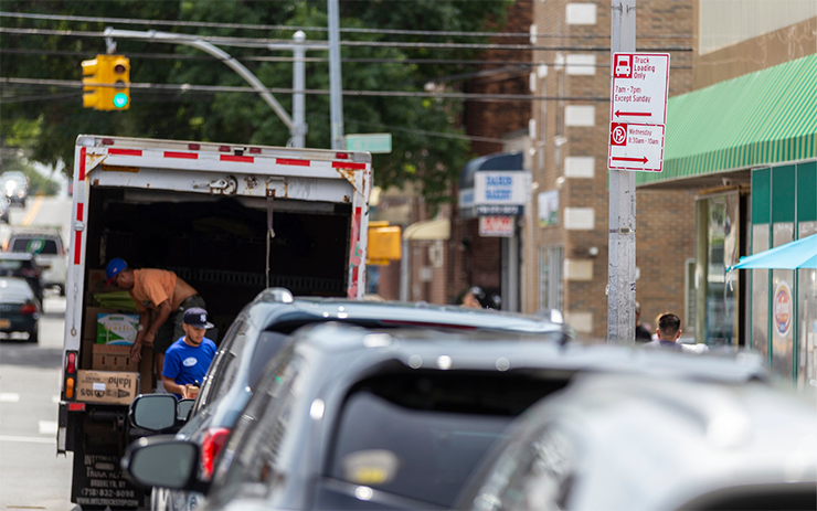 People unload boxes from a truck parked in a curbside parking space near a sign that reads Truck Loading Only.