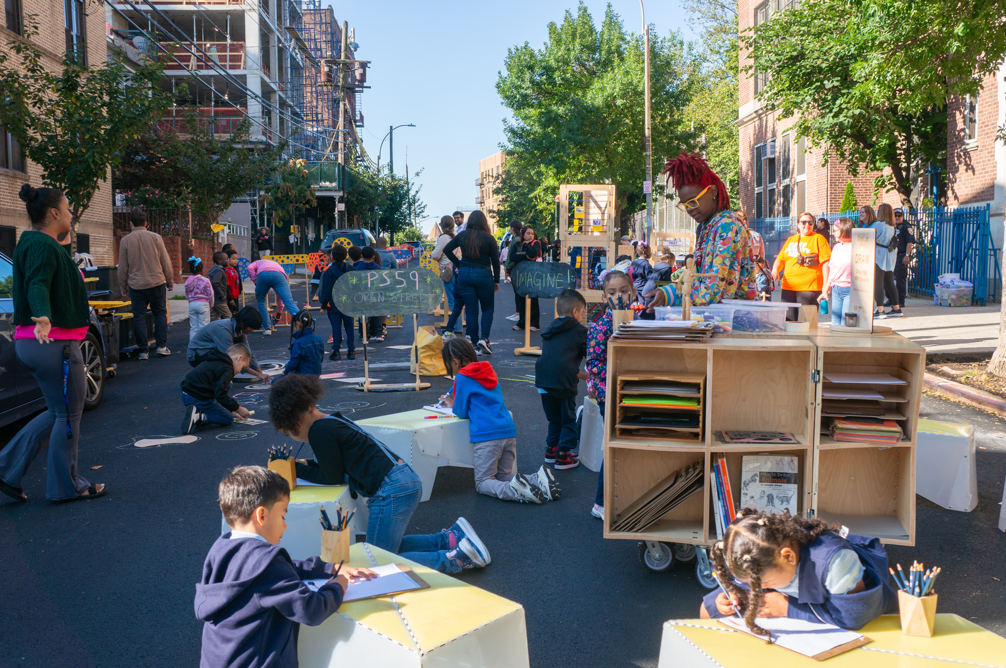 Children draw and color on a street closed to vehicular traffic.
