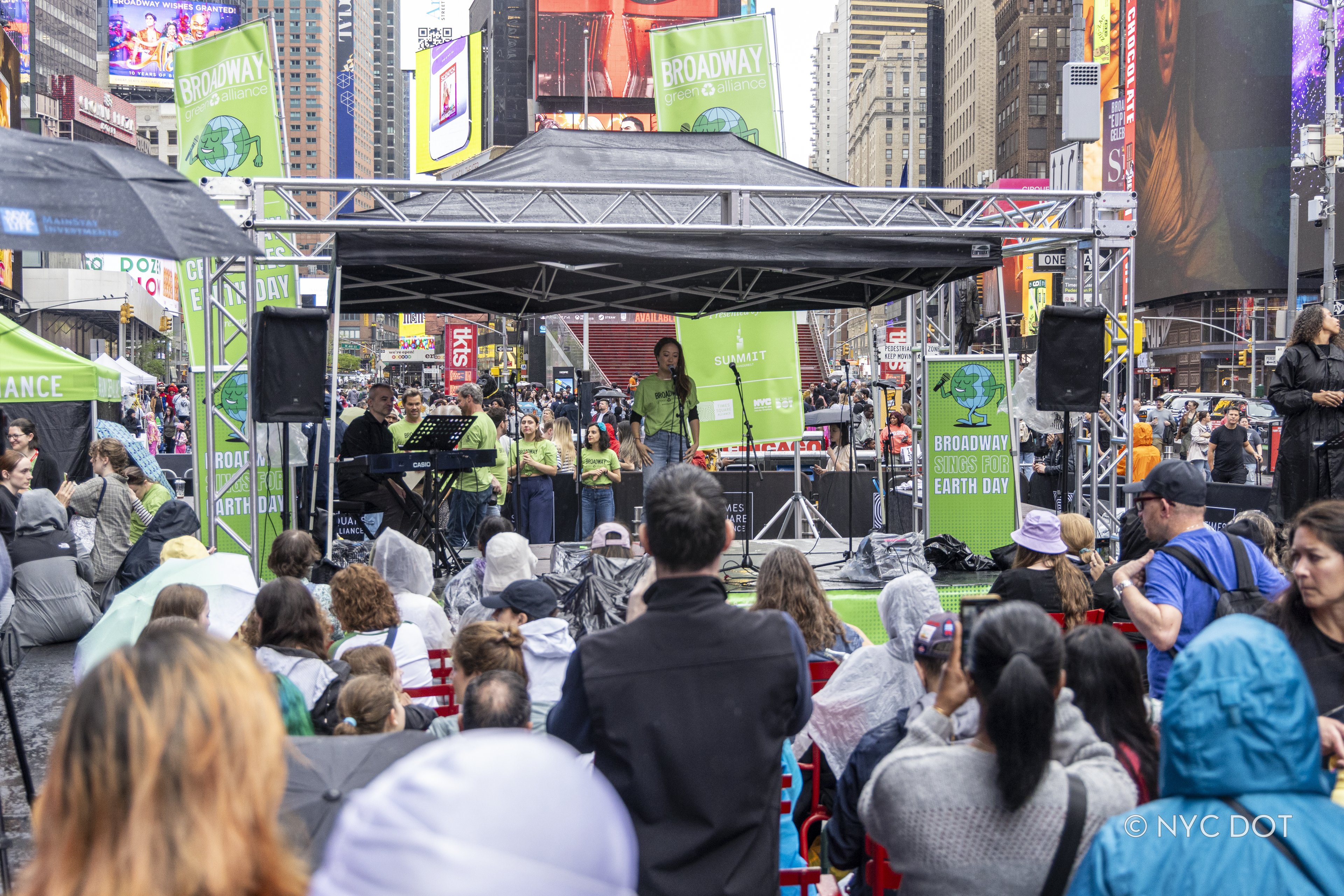 A large crowd watches a woman wearing green singing on a stage in Times Square.