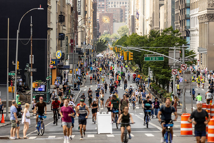 On a summer day in N Y C people run, walk and ride bicycles on a street closed to vehicle traffic.