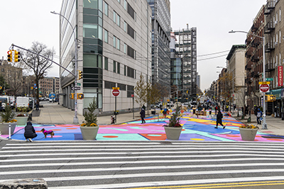 On a winter day, people walk over a colorful mural painted on a roadway closed to vehicular traffic in Washington Heights.