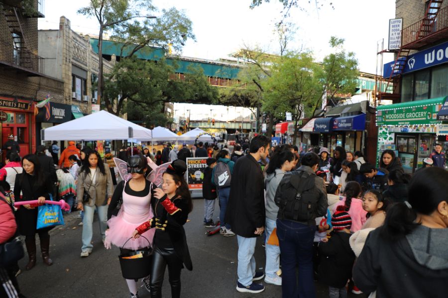 Multiple people, some in Halloween costumes, enjoy activities along a street closed to vehicular traffic.