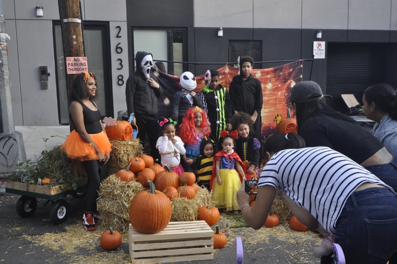 A family in Halloween costumes poses for a photo with pumpkins on a street closed to traffic in the Bronx