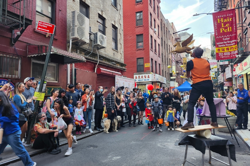 A crowd of people watches a circus performer on open street in Manhattan’s Chinatown