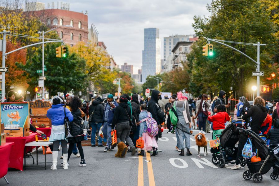Kids and adults and pets in Halloween costumes enjoy a street closed to vehicular traffic.