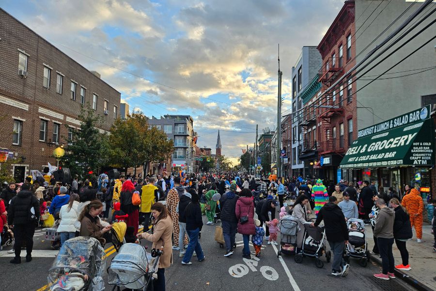 Multiple people walk along a street closed to vehicular traffic and participate in Halloween activities.