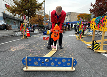 A young child dressed as pumpkin is helped by her father to walk on an obstacle course setup on a street closed to vehicles on Halloween.