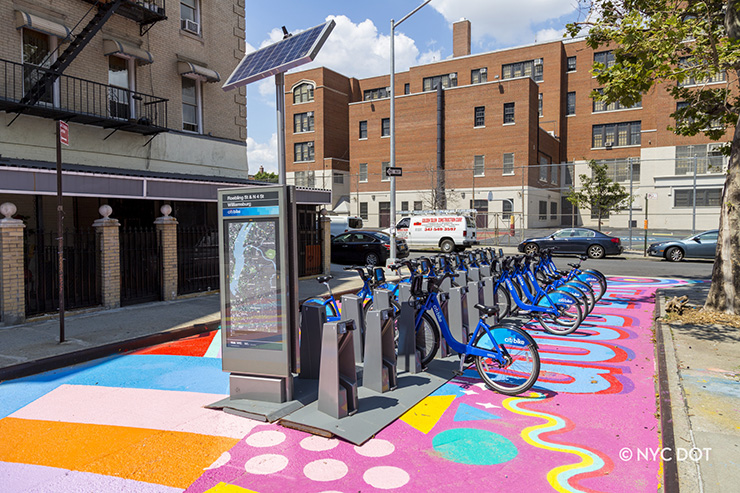 Citi Bike station with a solar panel and large neighborhood map is installed on a colorful street mural