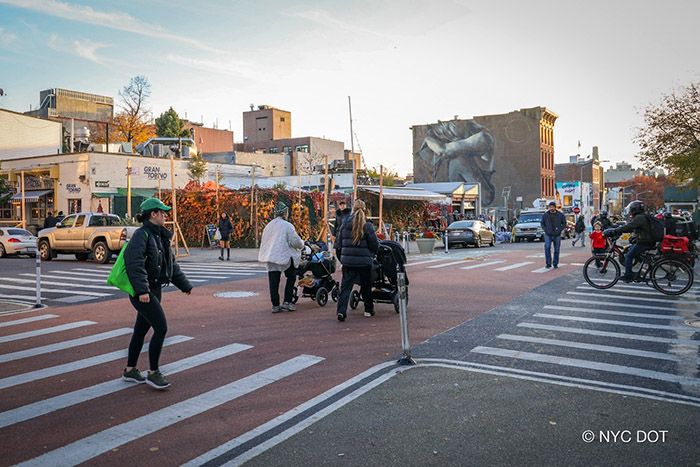 Multiple people walk and push strollers along the Berry Street Open Street.