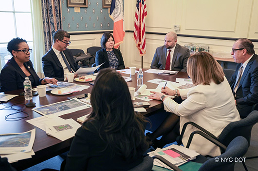 A group of people, including Commissioner Rodriguez, Council Members Hanks and Borelli and Borough President Fossella meet around a table covered in papers.