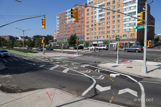 A wide boulevard in the Bronx has a new two-way green bike lane, new concrete pedestrian islands, and new lane and crosswalk markings.