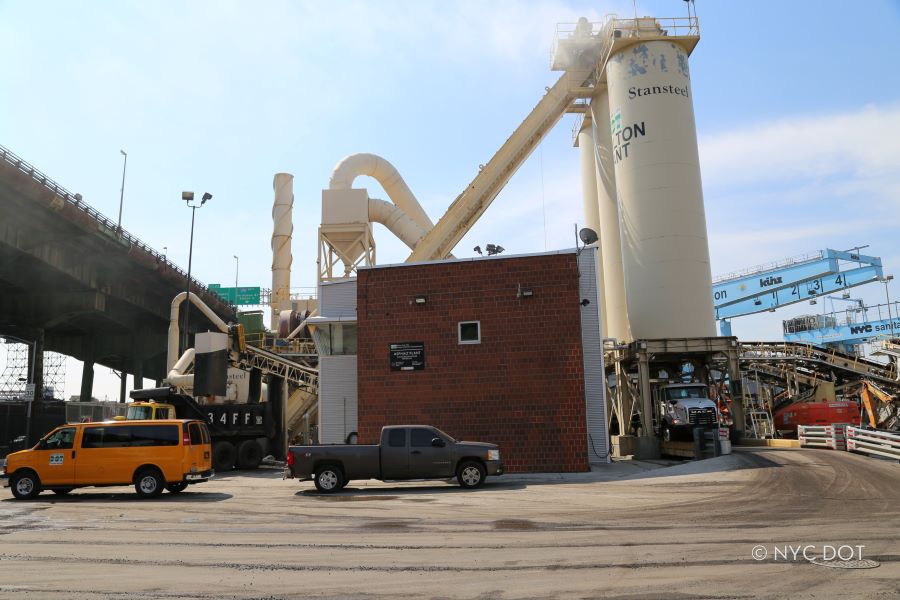 A picture containing truck, outdoor, at an asphalt plant. Text on the building says New York City D O T Hamilton Plant