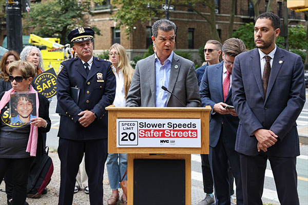 Commissioner Rodriguez speaks from behind a podium with a sign that says, Speed Limit 20 – Slower Speed Safer Streets.