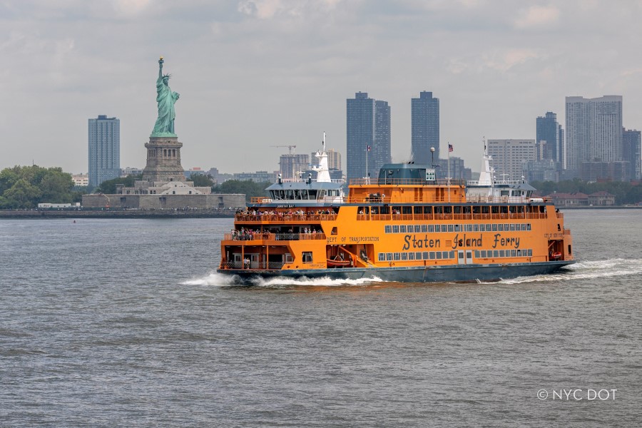 Orange Staten Island Ferry crosses the harbor with the Statue of Liberty and city skyline in the background.