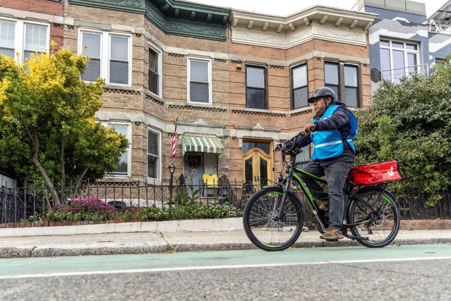 Food delivery worker on an e-bike in front of a row of houses.