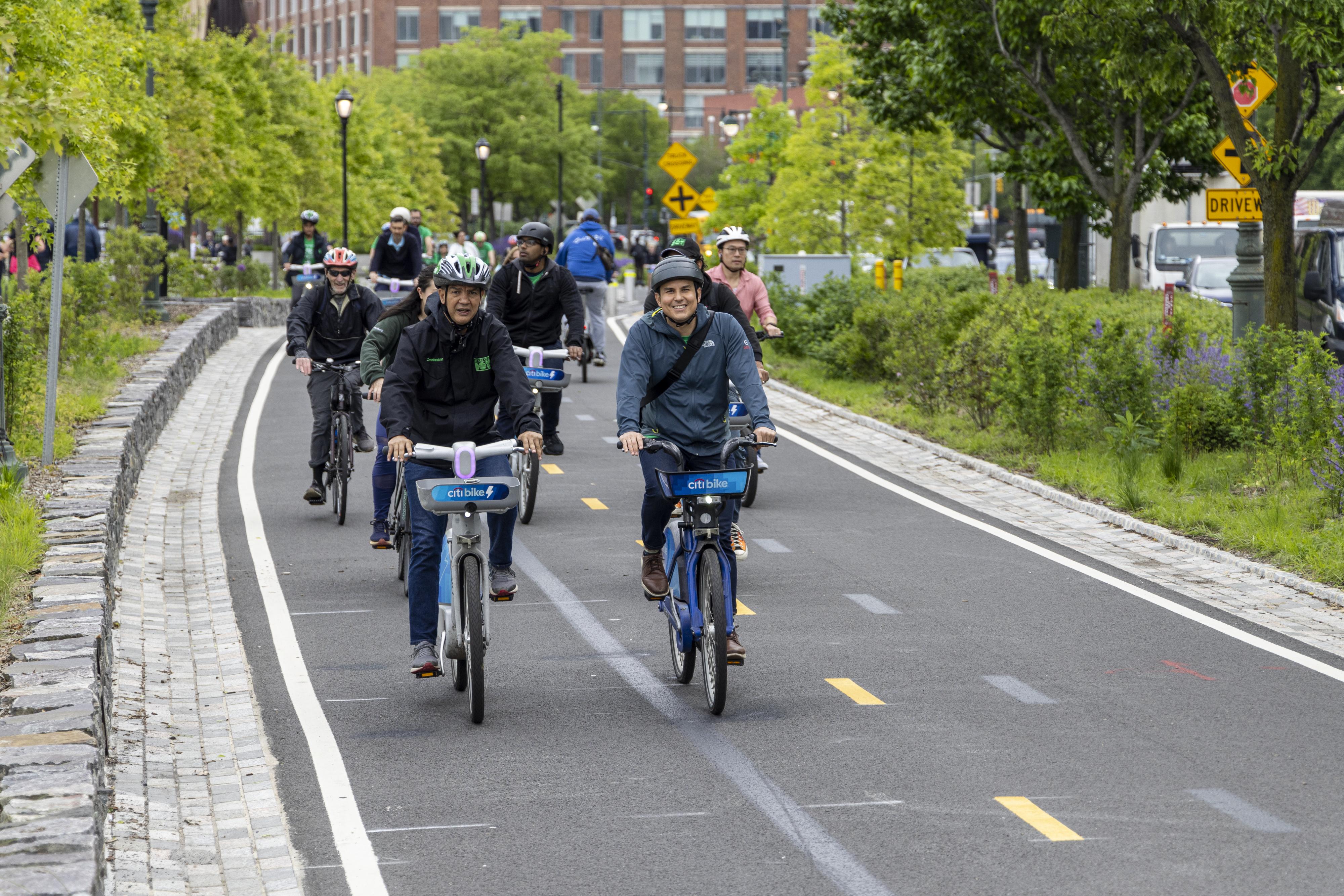 Multiple cyclists wearing helmets ride on a two-way bicycle lane.