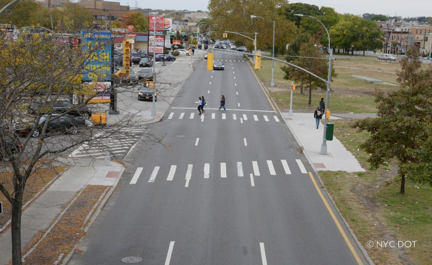 Pedestrians walk in a crosswalk across a wide roadway in Brooklyn.