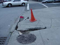 an orange cone rests on top of a sidewalk that has collapsed near the corner.