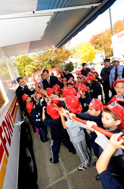 Director of the FDNY's Fire Safety Education Unit Lt. Anthony Mancuso (left), State Senator Andrew Lanza (center, with red tie) and children from P.S. 6 on Staten Island cut the ribbon that officially unveils the new fire safety Smoke House.