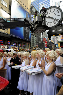 Hot Dog, the fire safety mascot, changes the clock for Daylight Saving Time at the Hilton in Times Square as Chief of Department Salvatore Cassano and Marilyn Monroe look-alikes stand below.