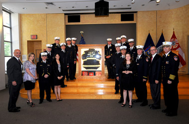Fire Commissioner Salvatore Cassano and Chief of Department Edward Kilduff join the FOMI graduates, and members of GE and Columbia. They stand in front of Chief Jonas's bunker coat that was given by the class as a gift to GE for their generosity. 
