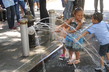 Children playing in a hydrant equipped with a spray cap.