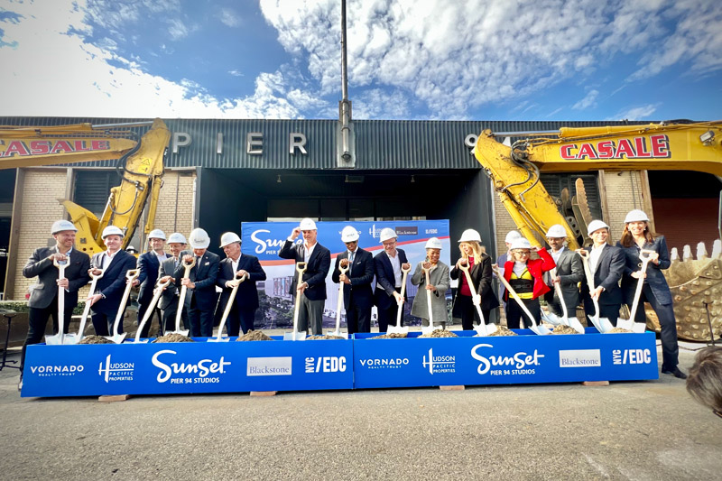 mayor adam in the middle along with other officials wear safety helmets and hold shovels
