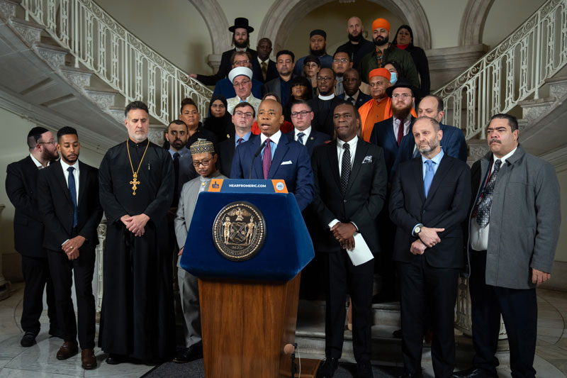 mayor adam is speaking at podium while faith-based leaders stand behind him.