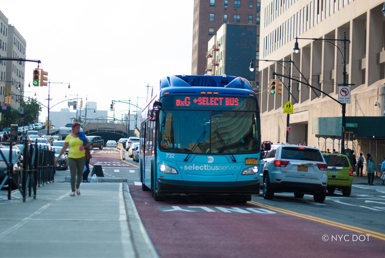 A bus is moving toward the frame, while a person walking  on sidewalk