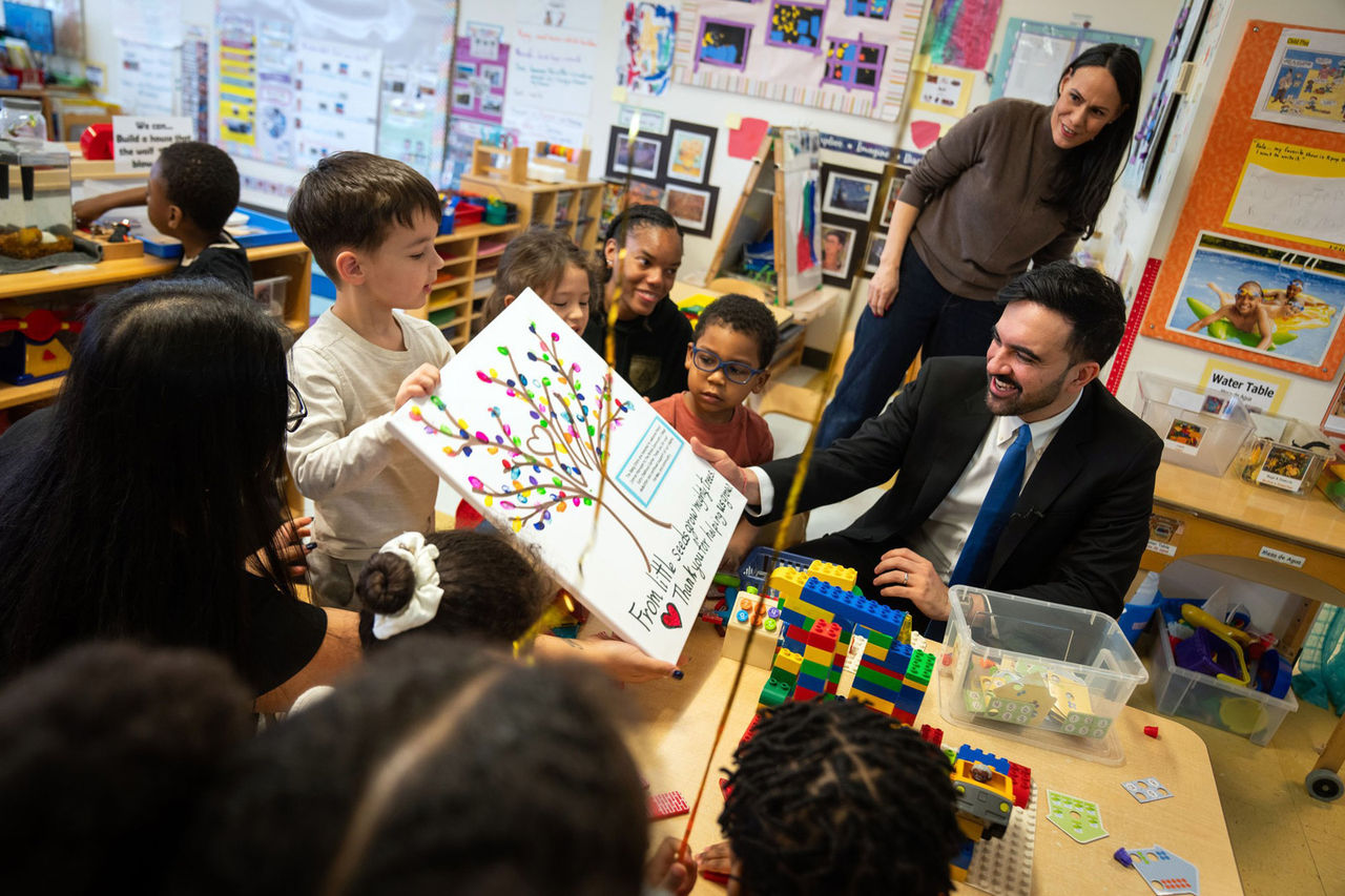 a kid is holding a drawing on a card board, while Mayor Mamdani is appreciating it.