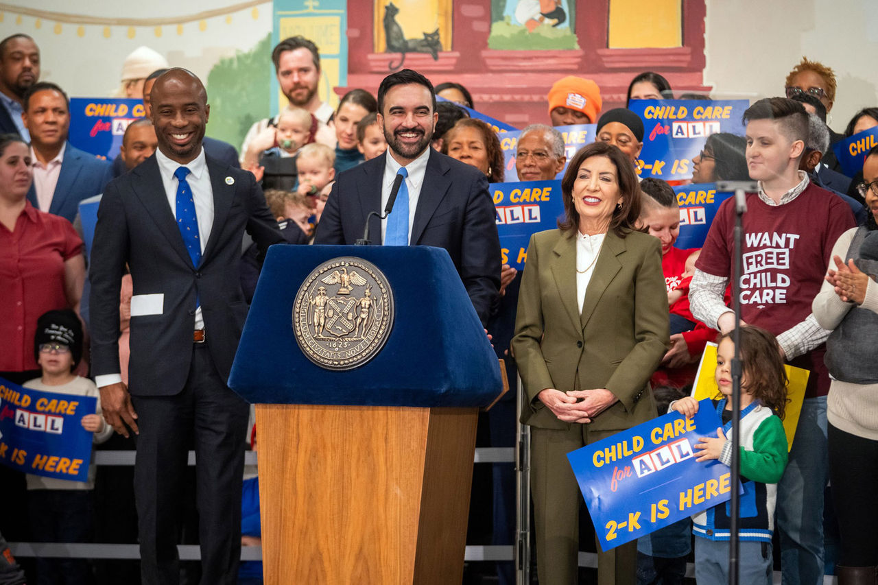 Mayor Mamdani at the podium center, is accompanied by Governor Hochul and DOE Commissioner, while a group people stand behind them