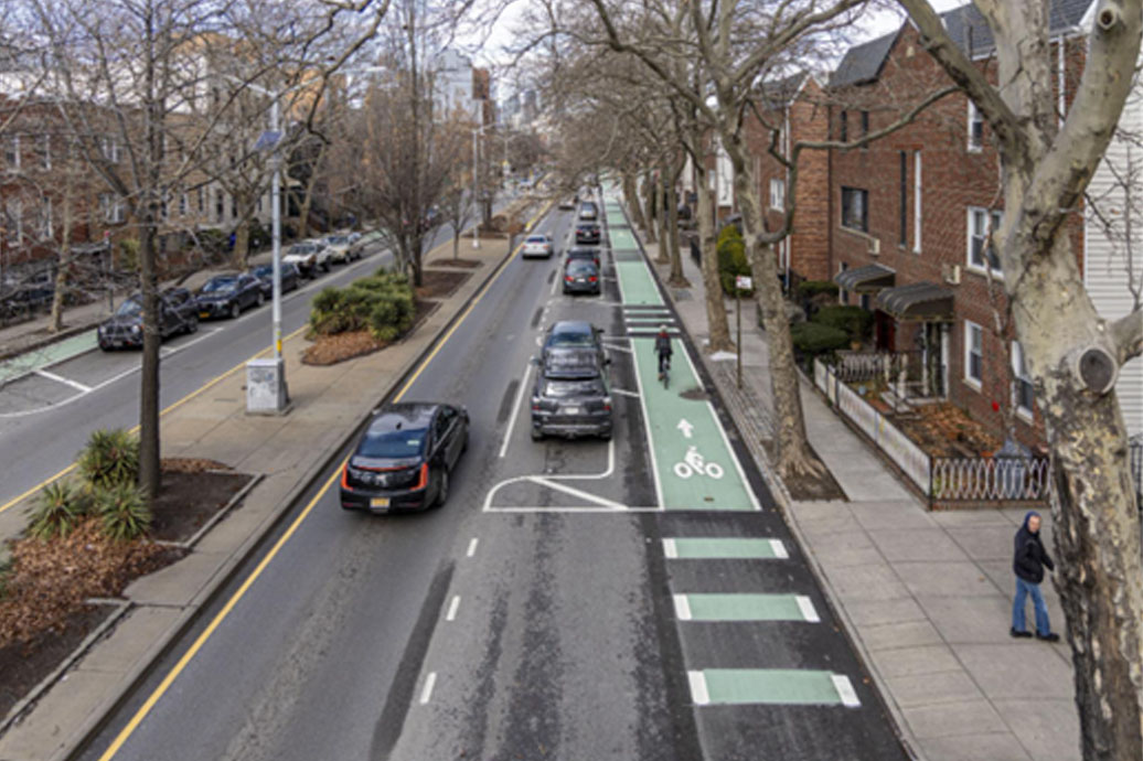 an aerial view of street with bike lane, cars are moving and passing by other cars