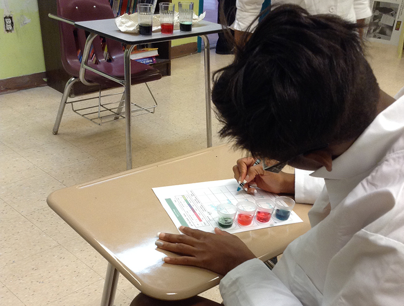 A young person is filling out a worksheet with a crayon while sitting in a classroom sitting.