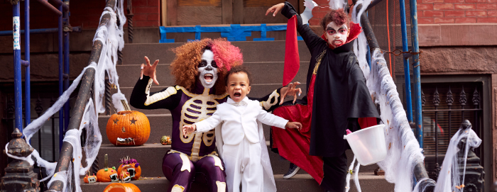 A person in a halloween costume with two children also dressed in halloween costumes in front of a staircase of a building