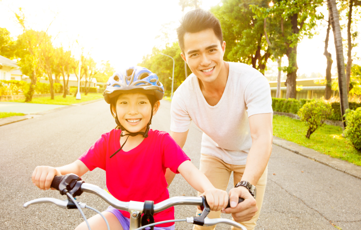 Person holding child on a bicycle. The child is wearing a helmet and a red shirt
                                           