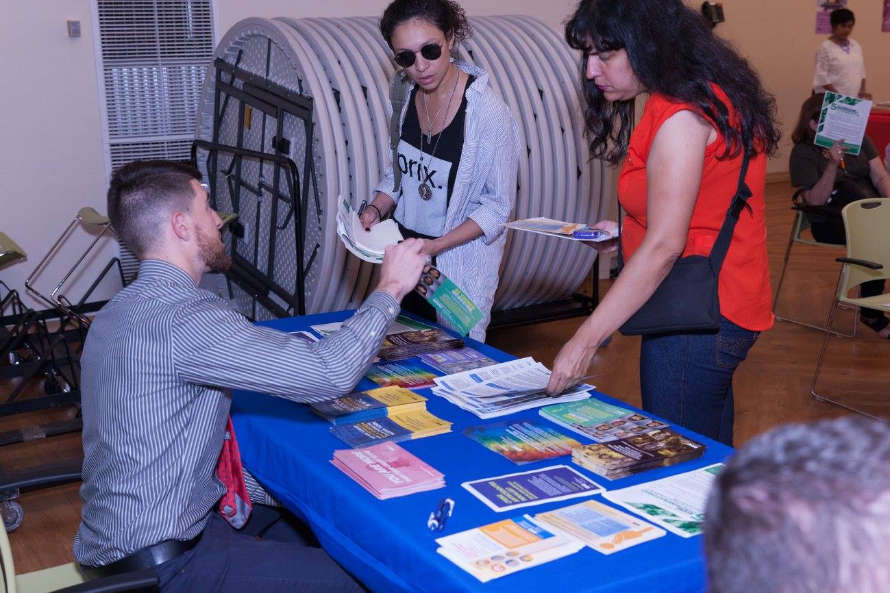 Commission staff member sitting at a table with materials, distributing literature to two New Yorkers.