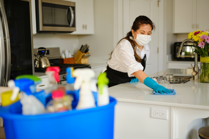 A professional housecleaner wiping down kitchen counter next to a bucket of clea
                                           