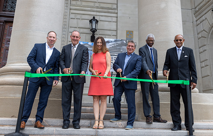 City officials five men and a woman all holding scissors to cut the green ribbon
                                           