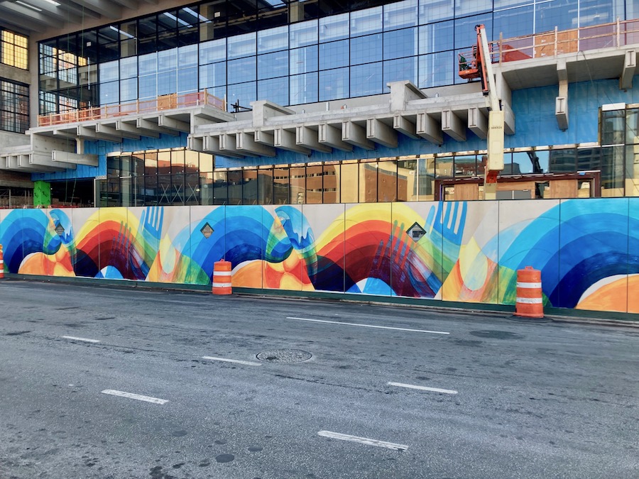 Photograph of a colorful mural by Tomashi Jackson painted on a sidewalk shed that depicts waves of banded colors and silhouetted hands.