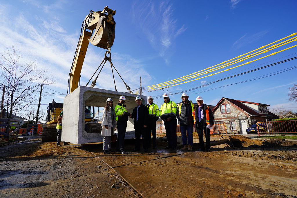 Employees of DEP and DDC shaking hands while standing in front of a large concrete box sewer
